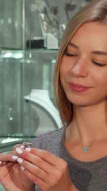 Uzun sarı saçlı ışıl ışıl genç bir kadın zarif bir elmas yüzüğü incelikle incelerken gülümsüyor. Etrafı lüks takılarla çevrili. Bu büyüleyici an, onun en güzel parçayı seçme heyecanını yakalar. Lüks hayatın neşesini somutlaştırır.