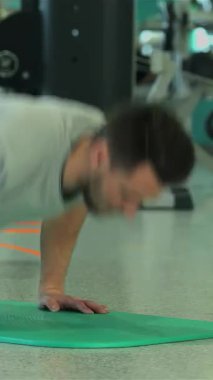 Orta Doğu kökenli kendini adamış genç bir adam canlı bir yeşil egzersiz minderinin üzerinde şınav çekerek fitness ve güç eğitimine olan bağlılığını somutlaştırıyor. Enerjik spor salonu atmosferi çeşitli çalışma ekipmanlarıyla canlıdır.