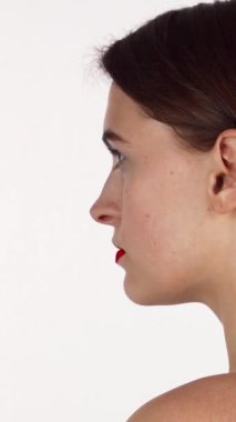 Büyüleyici kısa saçlı bir kadın kendine güvenen bir bakışla başını çevirir, büyüleyici cazibe ve entelektüellik saçar. Çarpıcı kırmızı ruju ve kusursuz cildi saf beyaz arka planda, modern güzelliğin büyüleyici bir portresini yaratıyor.