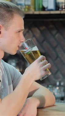 Parlak sarı saçlı şık beyaz bir adam soğuk bir bardak birayı kaldırırken neşeli bir şekilde ışıldıyor. Parlak bar tezgahına yaslanıyor. Bulaşıcı gülüşü ve gevşemiş tavırları güzel bir atmosfer yaratıyor.