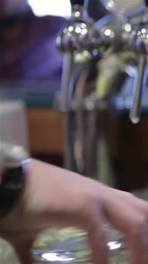 Yetenekli bir erkek barmen parlak bir musluktan keskin bir bira dökerek canlı gece hayatının özünü yakalıyor. Köpüklü bira serin bir bardağa dönüşürken ve susamış müşterileri doyurmaya hazırlanırken sahne enerji dolu.