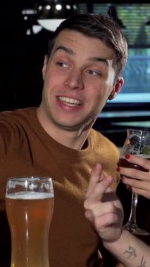 Neşeli bir arkadaş grubu akıllı bir telefonla selfie çekiyor. Kahkahaları rahat bar atmosferini dolduruyor. Yakışıklı adam, sıcak bir gülümseme ve bir bardak altın birayla neşeli bir kadınla arkadaşlığını kutluyor.