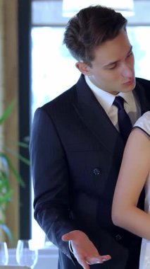 Zarif bir takım elbise giymiş çekici bir adam çekici bir kadına davetkar bir şekilde el kol hareketi yapar ve onu güzel bir restoran masasında kendisine katılmaya teşvik eder. Bu samimi sahne romantizm saçıyor, mum ışığı yanıp sönerken, ılık bir ortam yaratıyor.