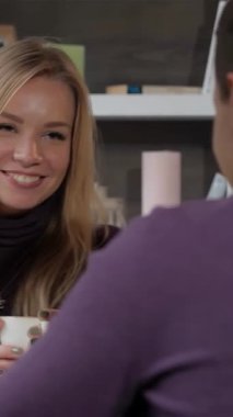 Parlak sarı saçlı genç bir kadın büyüleyici bir kafede erkek arkadaşıyla çay içerken kahkahalarla gülüyor. Çiçek aksanları ve sıcak ışıklandırmayla zenginleşen rahat ortam, hoş bağlantıları için samimi bir zemin oluşturur.