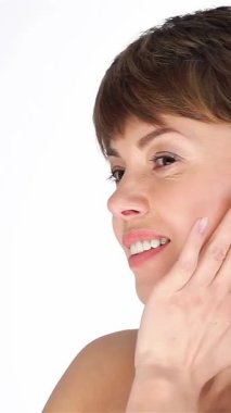 Işıl ışıl cildi parlayan orta yaşlı bir kadın yüzünü nazikçe okşar, kusursuz cildini el değmemiş beyaz bir arkaplanda gösterir. Bu büyüleyici portre güzelliği ve özgüveni temsil ediyor. Yaşlanmanın zarafetini kutluyor.