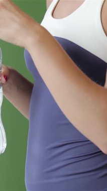 Azimli, canlılık dolu genç bir kadın enerjik bir yeşil spor salonunda yoga seansından sonra su şişesinden bir yudum alarak kendini tazeler. Onun dingin ifadesi ve şık atletik giysisi mükemmel bir fitness karışımı ve