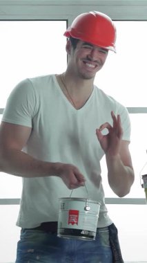 Güneşli, boş bir dairede, canlı turuncu kasklı iki hevesli işçi boya kutularını tutarken gururla başparmaklarını kaldırıyorlar. Bulaşıcı gülümsemeleri ve pozitif enerjileri takım çalışmasını ve adanmışlıklarını temsil ediyor.