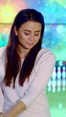 Neşeli genç Asyalı bir kadın canlı pembe bir bowling topu tutuyor, kendine güven ve heyecan saçıyor. Göz kamaştırıcı bir kozmik arkaplan karşısında bovling sahasında duruyor, oyunun heyecanını ve enerjisini somutlaştırıyor.