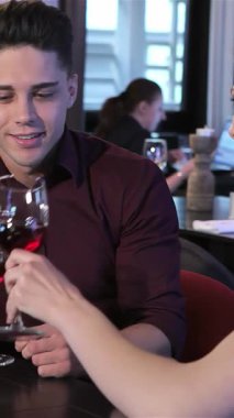 Şık bir restoranda, büyüleyici bir çift neşeyle kırmızı şarap kadehlerini tokuşturur, sıcaklık ve bağlantı yayar. Yakışıklı beyaz adam ve zarif kadın, gülücüklerle dolu romantik bir ortamda, parlak bir gülümsemeyi paylaşıyor.