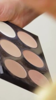 Yakından bakıldığında bir kadının elleri zarif bir şekilde parlak bir paletten canlı ruj sürerken, güzellik ve kendine güven yayarken görülüyor. Şık kuaför salonunun enerjik atmosferi dönüşümün heyecanını arttırıyor ve makyajın sanatını ön plana çıkarıyor.