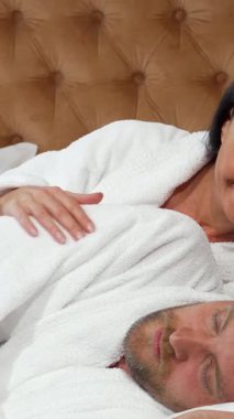 Sıcak, yumuşak bir yatak odasında olgun bir adam, ışıl ışıl beyaz bir bornoza sarılmış güzel karısının ışıl ışıl gülüşüne uyanır. Samimi sabah anları, şefkatle kolunu okşayarak sevgiyi ve bağlantıyı somutlaştırırken sıcaklıkla doluyor.