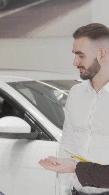 Kendine güvenen bir işadamı, parlak, modern araçlarla çevrili şık bir araba galerisinde bir satıcıyla dinamik bir konuşma yapar. Keskin giyinmiş genç erkek müşteri seçenekleri değerlendiriyor ve uzman tavsiyesi alıyor.