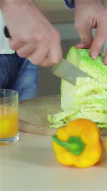 İki genç arkadaş, bir erkek ve bir kadın, taze sebzelerle çevrili, güneşli bir mutfakta canlı yeşil ve mor lahana dilimliyorlar. Sahne, parlak sarı biberler ve canlandırıcı bir bardak meyve suyuyla renklerle dolup taşıyor.