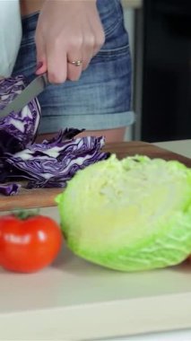 İki genç arkadaş, bir kadın ve bir erkek, taze sebzelerle dolu güneşli bir mutfakta canlı yeşil ve mor lahana dilimliyorlar. Canlı sahne, parlak kırmızı bir domates ve biber karışımının yer aldığı, renkle dolup taşıyor.