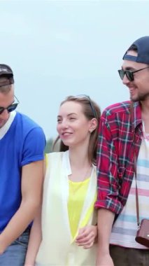 Üç şık genç arkadaş, birlikte parlak mavi bir gökyüzünün altında gülüşmeler ve sıcak gülümsemeler içinde, dostluk ruhunu somutlaştırarak dolaşıyorlar. Parlak kıyafetleri ve tasasız enerjileri, güneşin vurduğu bir ortam için mükemmel bir ortam yaratıyor.