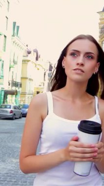 Göz kamaştırıcı genç bir kadın, elinde bir bardak tutarak eski bir kasabada geziniyor. Canlı binalar ve kaldırımtaşı sokaklar büyüleyici bir zemin oluşturuyor, neşe saçıyor ve macera hissi veriyor.