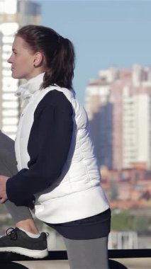 Odaklanmış genç bir kadın, göz kamaştırıcı bir şehir siluetine karşı kurulmuş, parlak bir yaya köprüsüne bacağını uzatıyor. Bu canlandırıcı sahne kentsel fitness ruhunu somutlaştırıyor. Güzelim bir sonbahar sabahında sağlığına ve canlılığına olan bağlılığını vurguluyor.