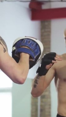 Enerjiyle dolu canlı bir spor salonunda, kararlı bir genç adam koçuyla antrenman yaparken güçlü yumruklar atıyor, hem odaklanma hem de yoğunluk saçıyor. Bu dinamik sahne profesyonel boksun özünü yakalar, acımasızlığı vurgular.