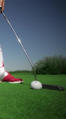 Kırmızı golf ayakkabıları giyen odaklanmış genç bir kadın, topla temas kurarken kararlılığını belli bir vuruşla ustalıkla ortaya koyuyor. Bereketli yeşil golf sahası, parlak güneş ışığı altında parıldıyor ve heyecan verici bir şey yaratıyor.