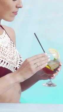Şık bikinili neşeli bir kadın köpüklü havuzun yanında, taze meyvelerle süslenmiş lezzetli bir kokteylin tadını çıkarıyor. Güneş ışığı su üzerinde parıldıyor, rahatlamayla ve mutlulukla dolu canlı bir yaz vahası yaratıyor.