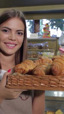 Büyüleyici bir yakın plan çekiminde hoş önlüklü genç bir kadın hasır sepetinden taze pişmiş kruvasanların enfes kokusunu soluyor. Onun ışıltılı gülümsemesi ve şakacı parmak öpme hareketi saf neşe saçıyor.