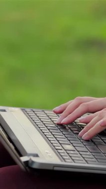 Neşeli bir kız, canlı bir şehir parkının yemyeşil yeşilliklerinin arasına kurulmuş dizüstü bilgisayarıyla derinden ilgilenir. Bu canlı sahne gençlik enerjisi yayıyor ve sıcak güneşin ve temiz havanın tadını çıkarırken verimli bir boş zamanın mutluluğunu.