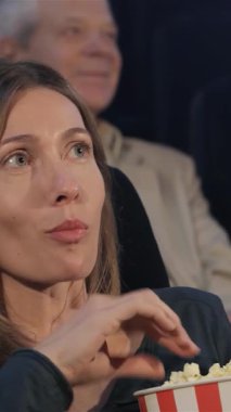 Uzun saçlı çekici bir beyaz kadın, canlı bir tiyatroda film izlerken gözleri heyecanla parlayan patlamış mısırdan keyif alır. Sinema izleyicilerinin kahkahalarıyla hareketli atmosfer, keyifli bir sahne yaratıyor.