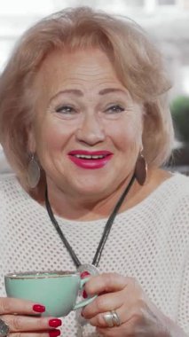 Ilık bir gülümsemesi ve canlı pembe rujuyla ışıl ışıl kıdemli bir kadın, sıcak bir kafede sıcak bir fincan çay içerken kızıyla kahkahalarını paylaşıyor. Bu iç açıcı sahne, neşe ve şefkat dolu ailenin derin bağını güzel bir şekilde gösteriyor.