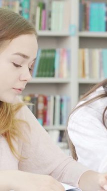 Kendini işine adamış iki genç kız, renkli kitaplıklar ve parlak dekorlarla çevrili, canlı bir kütüphanede derinden çalışmalarına devam ediyorlar. Odaklanmış ifadeleri ve işbirlikçi ruhları öğrenmenin sevincini ve arkadaşlığın gücünü vurgular.