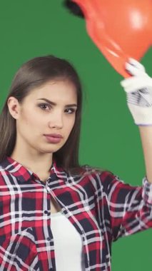 Kendine güvenen genç bir kadın müteahhit, canlı turuncu bir kaskı ve şık eldivenleri olan, çarpıcı yeşil renkli arka planına başparmak işareti veriyor. Neşeli gülüşü güç ve profesyonellik yayıyor, dinamik ruhunu sergiliyor