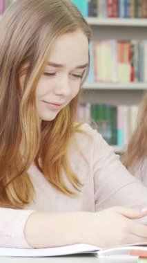 Üç neşeli genç kız, akıllı telefonlarına dalmış, rahat bir okul kütüphanesinde bulaşıcı bir kahkahayı paylaşıyorlar. Canlı yoldaşlıkları sıcaklık saçıyor, renkli kitaplıklar arasında dostluğun ve işbirliğinin güzelliğini vurguluyor.