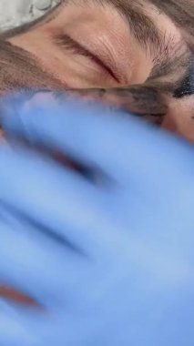 Sakin bir güzellik kliniğinde, yetenekli bir güzellik uzmanı yakışıklı erkek müşterilerinin yüzüne canlandırıcı siyah bir maske takarak cilt bakımı ritüelini geliştirir. Bu samimi sahne, karbon soymanın rahatlatıcı özünü yakalar, derinlere daldırır.