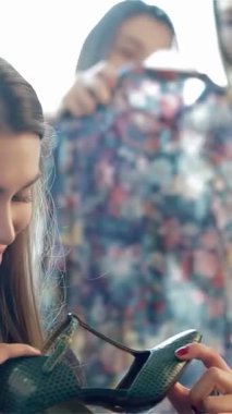 Keyifli bir kız bir çift şık ayakkabıya bakar, arkadaşı arka planda canlı çiçekli bir elbiseyi keşfederken gözleri heyecandan parıldar. Bu dinamik alışveriş anı arkadaşlığın özünü ve moda keşiflerinin heyecanını yansıtıyor.