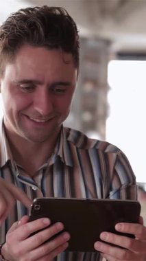 Rahat bir kafede, üç genç adam bir tabletin etrafında toplanıyor, yüzleri sevinçle parlıyor ve heyecan verici haberleri paylaşıyorlar. Titreşimli atmosfer yoldaşlık ve bağlantıyla uğulduyor, her anı canlı ve canlı hissettiriyor.