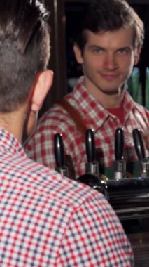 Çekici bir genç adam canlandırıcı bir biradan zevk alır, şık bir barda bir arkadaşıyla canlı bir sohbet eder, parlak ahşap ve musluklar sıcak, davetkar bir atmosfer yaratır. Konuşmalarının enerjik enerjisi neşe ve dostluk yayıyor.