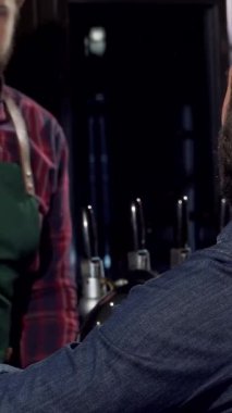 Tanınmayan bir adam zengin bir zanaat birasından zevk alır, barın canlı atmosferinin tadını çıkarırken bardağı nazikçe tutar. Yeşil önlüklü dost canlısı barmen içki servisi yaparken, parlayan ahşap ve hafif ışıklandırma içkileri sarıyor.