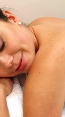 Yetenekli bir masör bir kadının sırtında sihrini konuşturur ve onu sakin bir spa atmosferiyle sarar. Neşeli beyaz kadın, parlak gülüşü ve yumuşak esmer saçlarıyla, hafif vuruşlardan zevk alıyor, saf rahatlık ve sağlığın somutlaştırılmış hali.