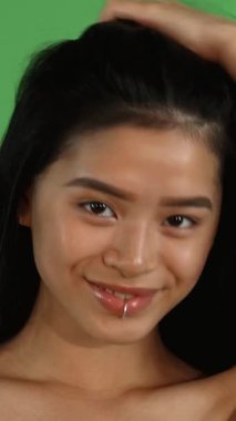 Bu canlı stüdyo portresi çarpıcı bir dudak halkası ile neşeli genç bir Asyalı kadını yakalıyor, uzun, parlak saçlarını canlı yeşil bir krom arka planda şaklatarak çeviriyor. Işıl ışıl gülüşü ve anlamlı gözleri kendine güven ve cazibe yayıyor.