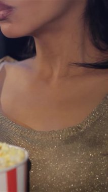 Şık bir siyah kadın, sinemanın büyüsüne tamamen dalmış bir parça tereyağlı patlamış mısırı dudaklarına doğru nazikçe kaldırır. Yakın çekim, onun ışıltılı gülümsemesini ve tiyatronun sıcacık parıltısını gözler önüne seriyor. Sinema gecesinin neşeli atmosferini güçlendiriyor.