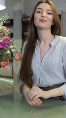 Genç, büyüleyici beyaz bir çiçekçi zarif bir şekilde masasına yaslanmış, hareketli çiçekçisinde sıcaklığını ve yaratıcılığını sergiliyor. Göz kamaştırıcı renkli çiçeklerle çevrili güzel kahverengi saçları, davetkar bir şekilde gülümserken zarifçe çağlıyor.