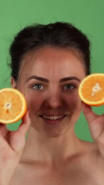 Neşeli genç bir kadın mutluluk saçıyor, parlak turuncu yarımlar sergiliyor. Canlı yeşil bir zemin üzerinde. Bu büyüleyici görüntü sağlık ve canlılık ruhunu somutlaştırıyor, taze, besleyici meyvelerin ve güzelliğin neşesini kutluyor.