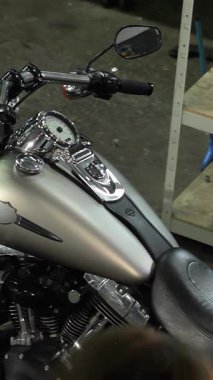 Çarpıcı bir bayan motorcu, canlı bir motosiklet atölyesinde parlayan bir helikoptere poz verirken kendine güveniyor. Bu büyüleyici yüksek açılı çekimde, şık siyah deri ceketli, şehvetli kıvırcık saçlı, çarpıcı beyaz bir kadın sergileniyor.