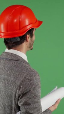 Parlak turuncu başlıklı erkek mühendisin dinamik arka görüntüsü canlı yeşil renkli bir ekrana doğru ustalıkla işaret ediyor. Bu büyüleyici sahne, ileri teknoloji ve yenilikçi mühendisliğin birleşiminin vücut bulmuş halidir.