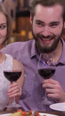 Hoş bir nişanlı çift, romantik bir akşamda, sıcak ve davetkar bir restoranda şarap kadehlerini tokuşturup, aşklarını kutluyor. Yumuşak, ortam aydınlatması, gülen yüzlerinde altın bir parıltı bırakıyor, neşe ve bağlantıyı vurguluyor.