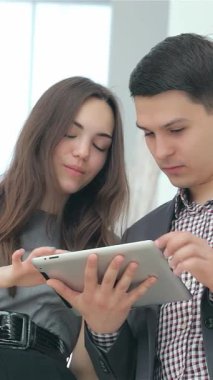 Heyecanlı genç bir çift, keskin iş kıyafetleri içinde, parlak bir tablet üzerinde etkileyici sonuçları hevesle gözden geçiriyorlar, heyecan ve takım çalışması yayıyorlar. Işıl ışıl gülüşleri ve meşgul ifadeleri girişimciliğin canlı enerjisini parlak bir şekilde yakalıyor.