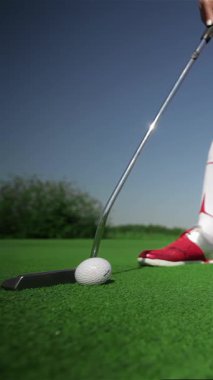 Yakından çekilen bir fotoğrafta, golf topuna canlı yeşil bir sahada vurmaya hazırlanan kararlı beyaz bir kadın görülüyor. Şık kırmızı ayakkabıları yemyeşil çimlerle çok güzel zıt düşüyor. Parlak yaz güneşinin altında, atletizmi somutlaştırıyor ve