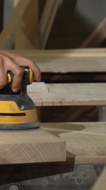 Odaklanmış bir erkek marangoz, canlı atölyesinde, bir dizi alet ve kereste ile çevrili, güçlü bir rastgele yörünge zımparalayıcısı ile pürüzsüz bir tahta parçasını tutkuyla parlatır. Bu canlı sahne, işçiliğin sanatsallığını simgeliyor.