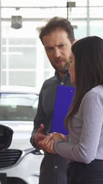 Gösterişli, modern bir galeride, deneyimli bir araba satıcısı genç bir kadına zarif bir şekilde kırmızı bir aracın kapısını açar ve onu içeri davet eder ve lüks bir deneyim yaşar. Parlak, havadar uzay heyecanla uğulduyor.