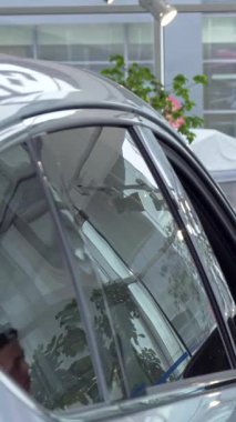 Yakışıklı genç bir adam derin düşüncelere dalıp modern bir bayilikte şık bir arabaya bakarken çenesini ovuşturuyor. Parlak, parlak sergi salonu, canlı bitkiler ve parlak araçlarla süslenmiş, davetkar bir atmosfer yaratır, heyecanı güçlendirir.