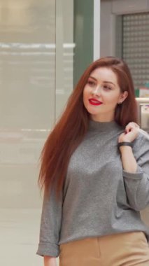 Işıl ışıl kumral saçları ve parlak bir gülümsemesi olan ışıl ışıl genç bir kadın, şık alışveriş merkezinin arka planında şık alışveriş çantalarını sıkıca tutarak rahatça poz veriyor. Bu canlı sahne, onun şık kıyafetinin altını çizerek perakende terapisinin heyecanını temsil ediyor.